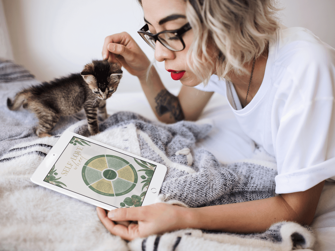 A woman with a kitten looking at the Self-Love Wheel on a tablet